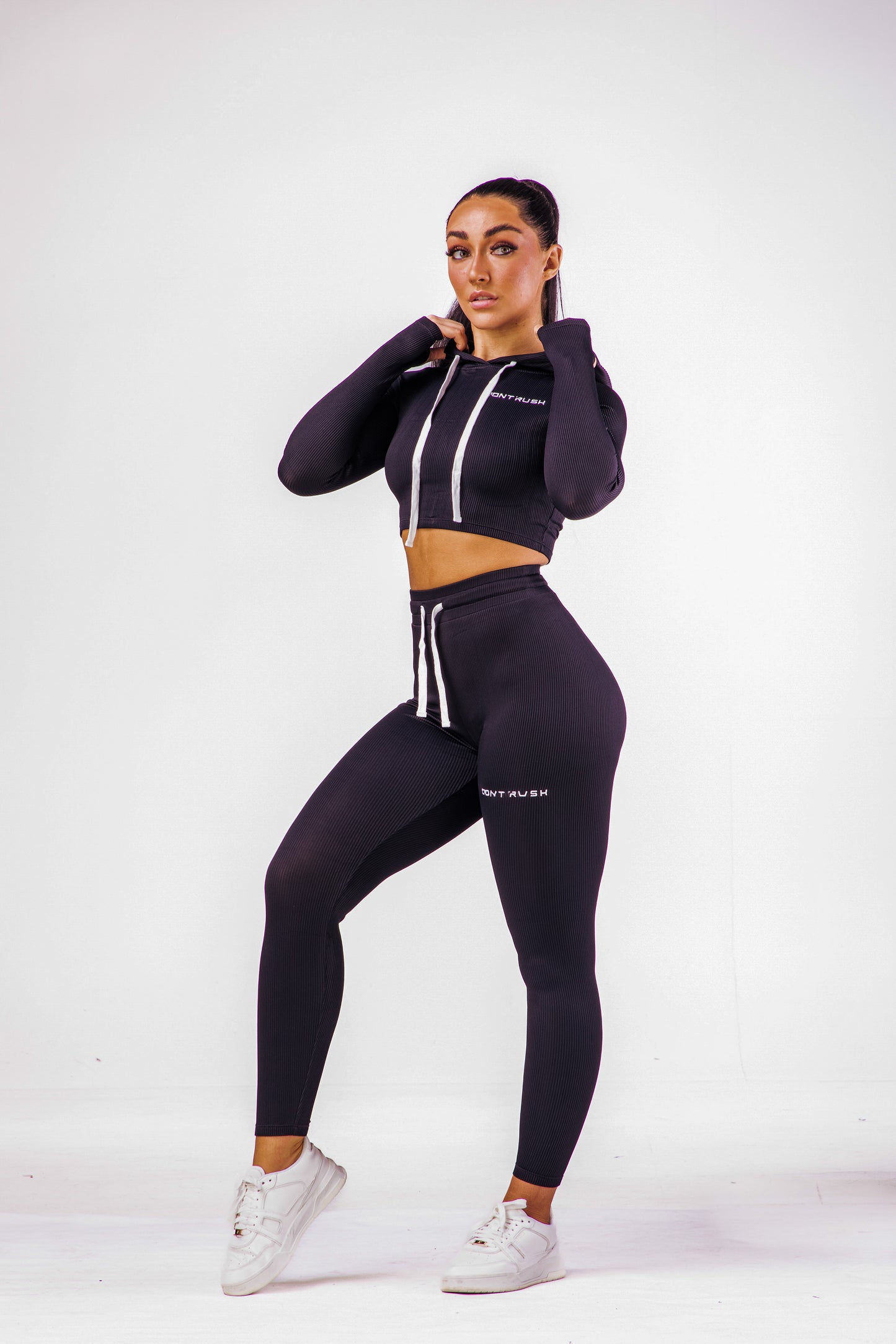 A woman wearing a black coloured gym high waisted leggings with a matching long sleeve cropped top with hoodie
