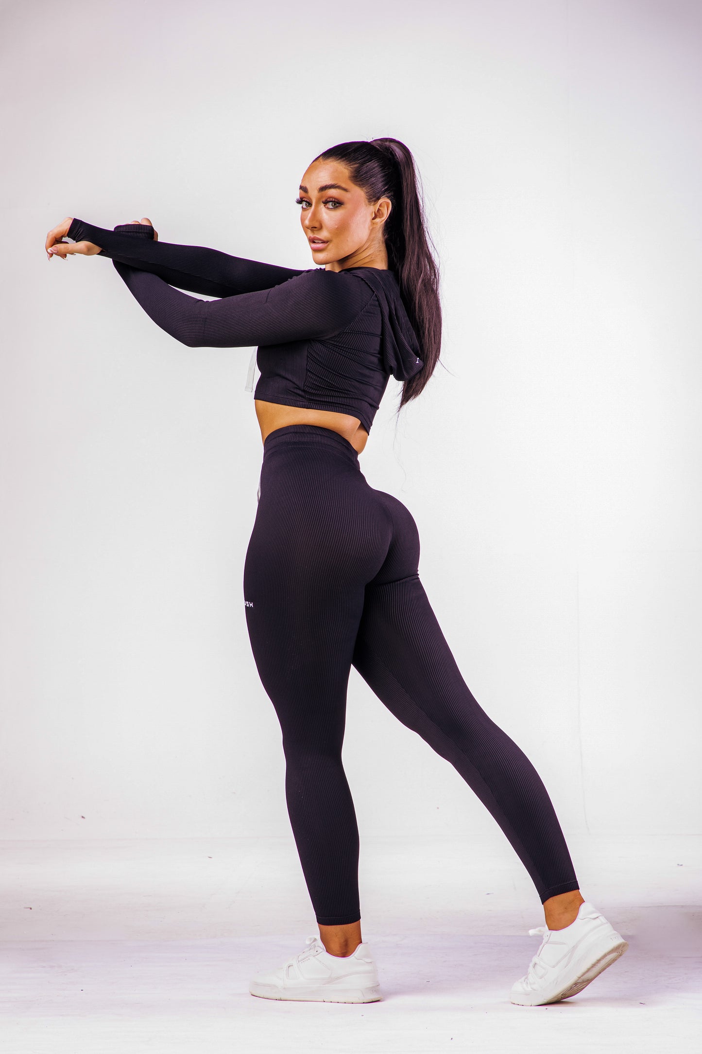 A woman wearing a black coloured gym high waisted leggings with a matching long sleeve cropped top with hoodie