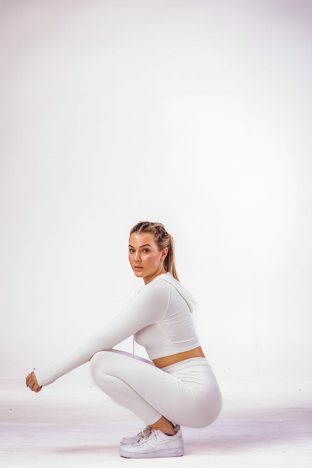 A woman wearing a white coloured gym high waisted leggings with a matching long sleeve cropped top with hoodie