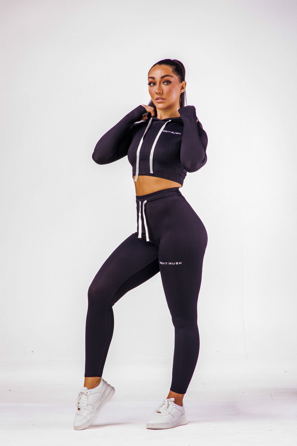 A woman wearing a black coloured gym high waisted leggings with a matching long sleeve cropped top with hoodie