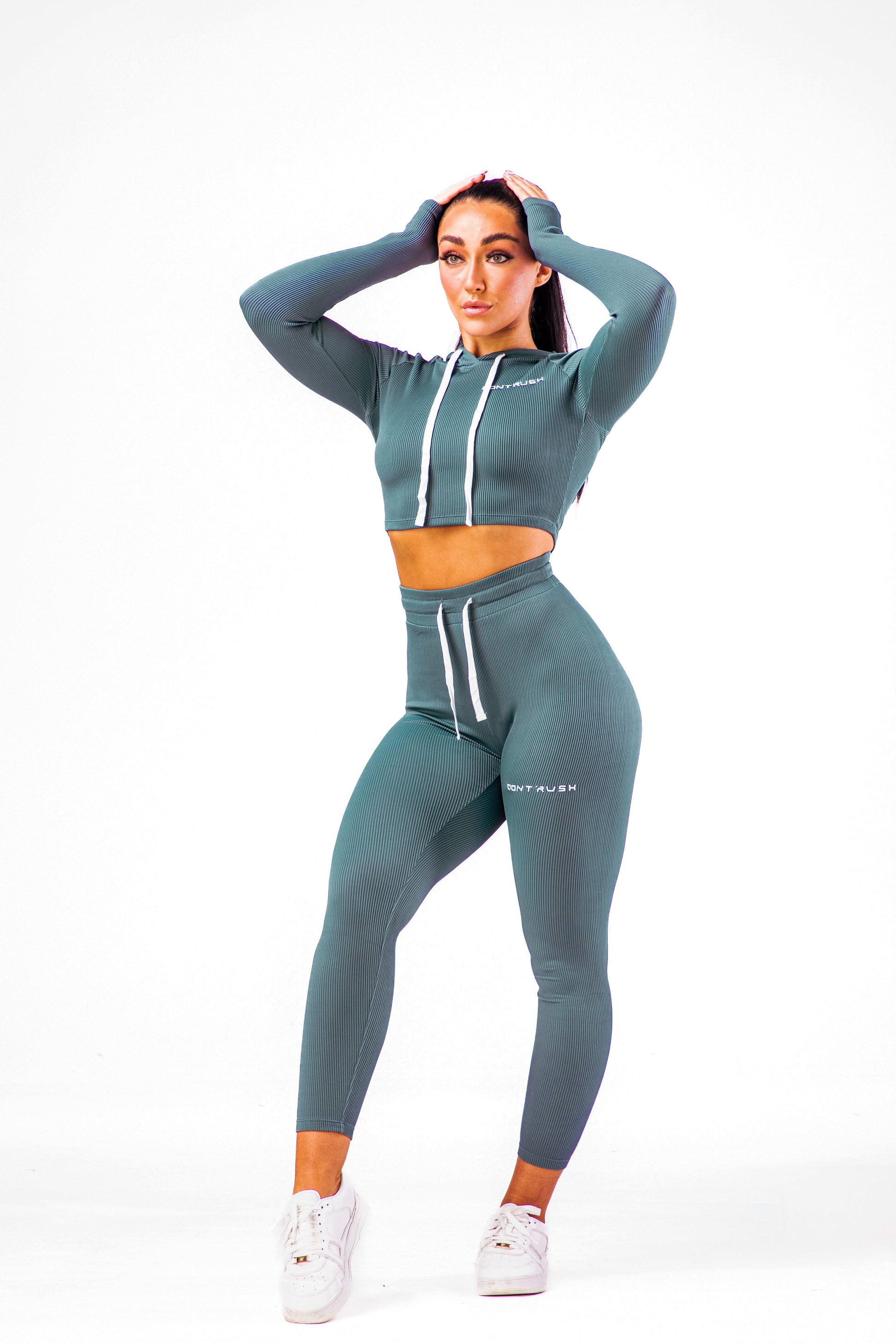 A woman wearing a dark teal coloured gym high waisted leggings with a matching long sleeve cropped top with hoodie