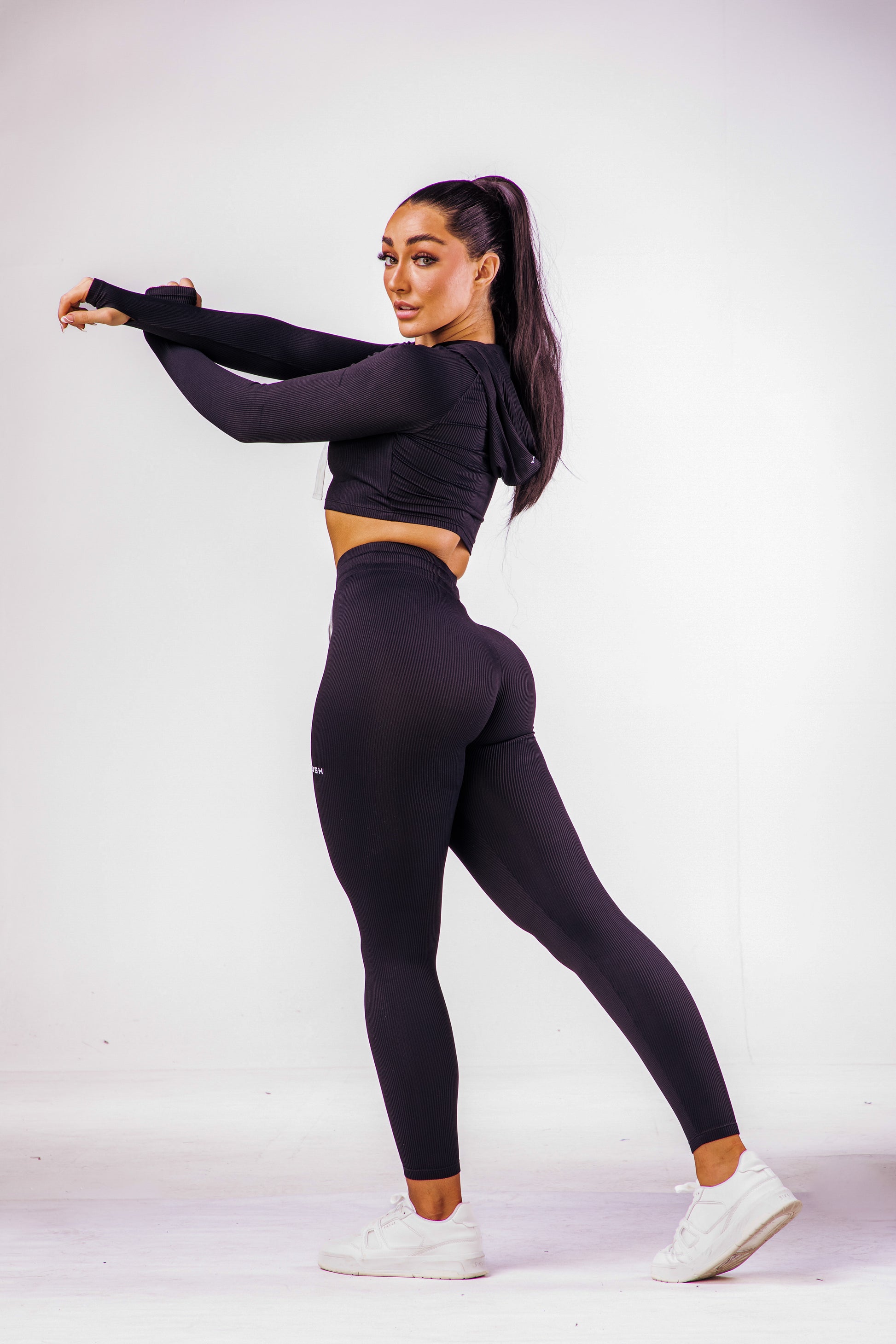 A woman wearing a black coloured gym high waisted leggings with a matching long sleeve cropped top with hoodie